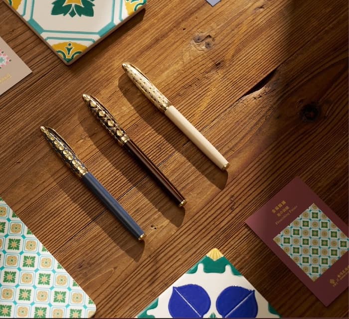 Three elegant fountain pens with gold-toned ornate caps and blue, brown, and cream colored barrels on wood.