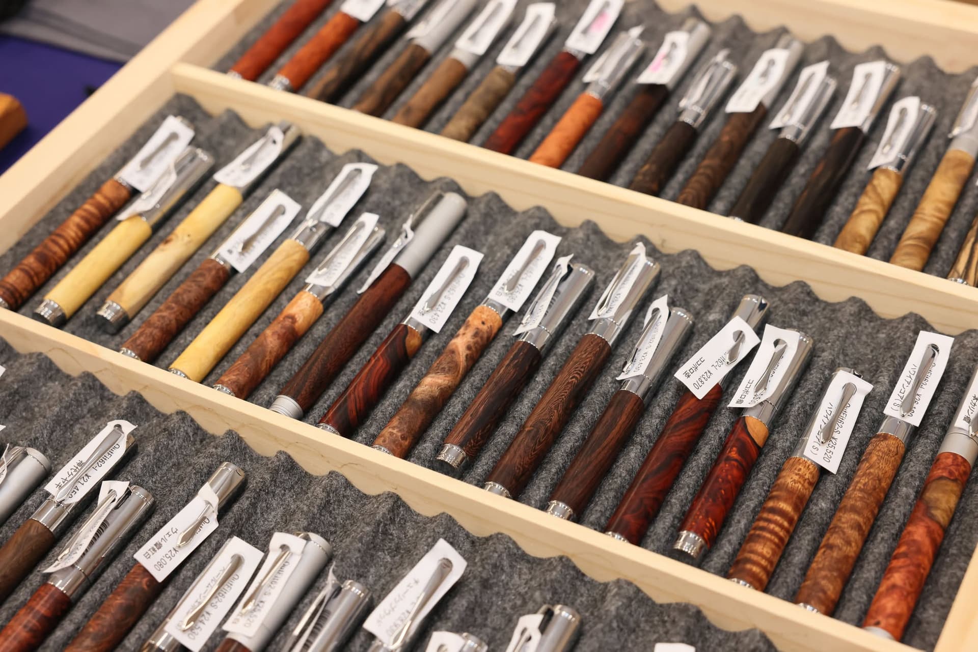 A collection of various handcrafted wooden fountain pens with silver clips displayed in a wooden tray.