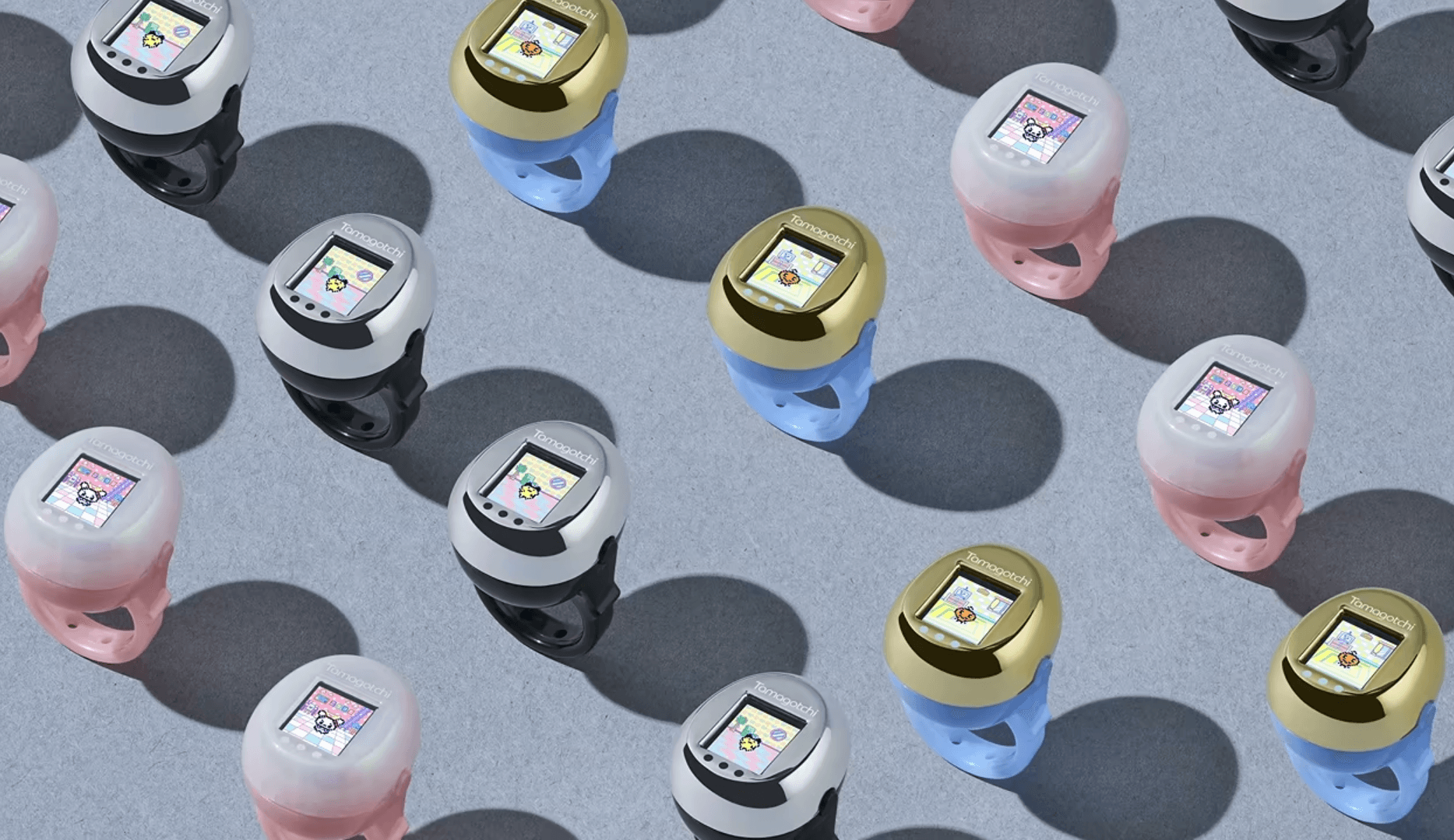 Assorted Tamagotchi rings in black, pink, and blue with gold accents arranged on a light grey surface.