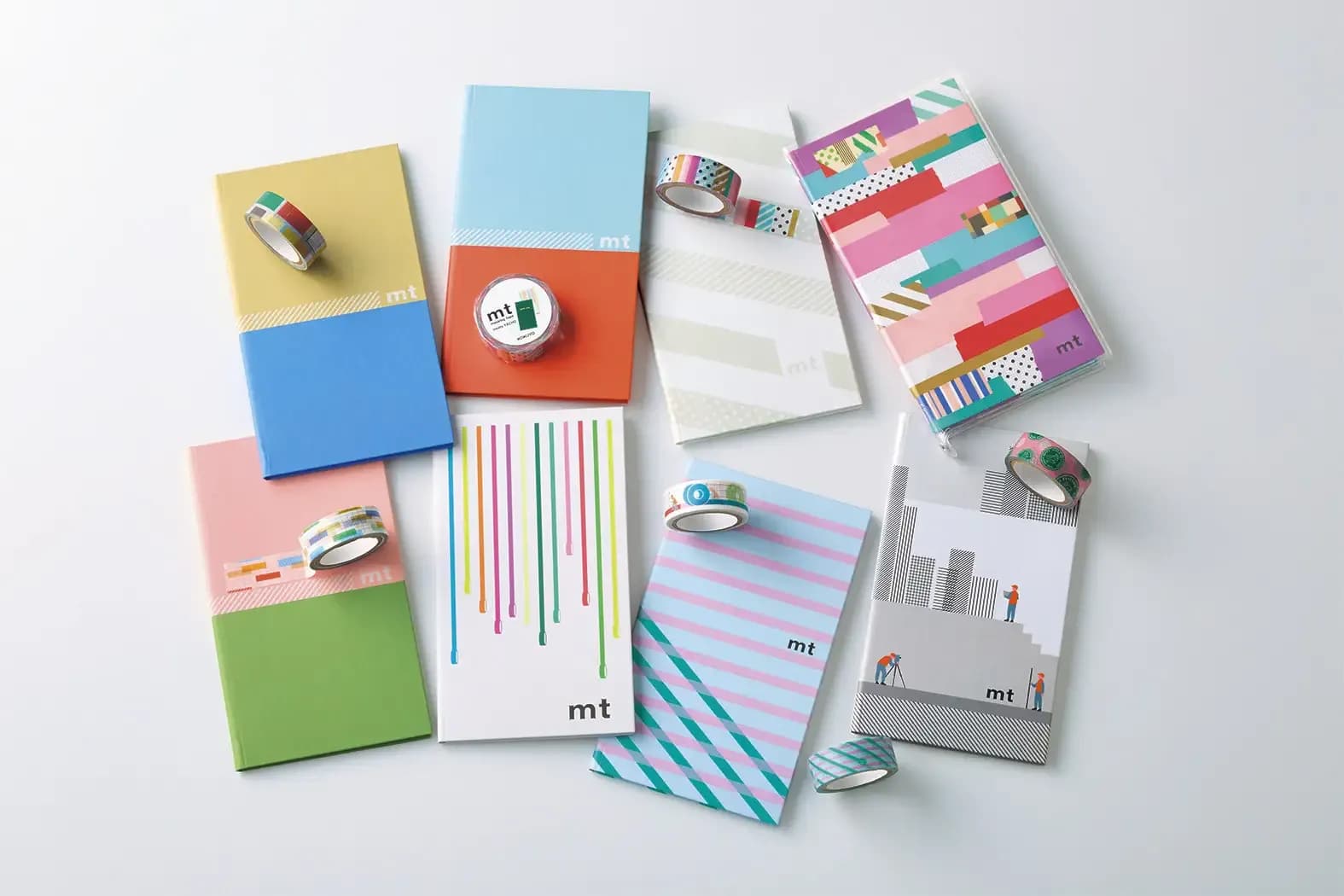 Assorted mt masking tape rolls and colorful patterned notebooks arranged on a plain white background.